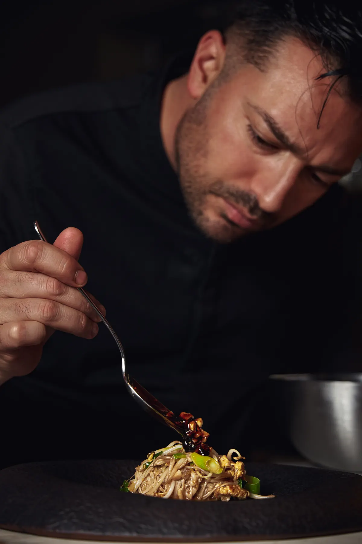 Chef termina un plato con cuchara sobre plato negro