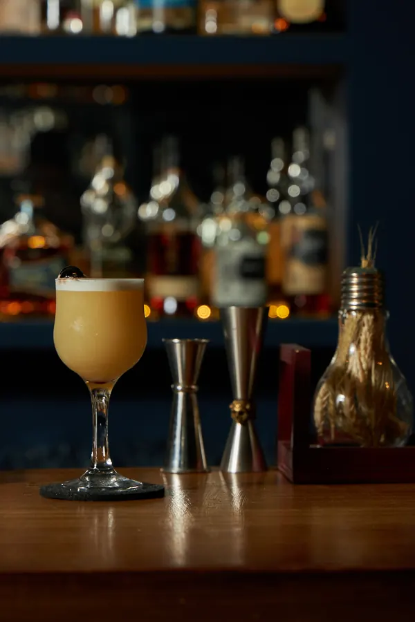 Cóctel con espuma en la barra, con las botellas iluminadas detrás