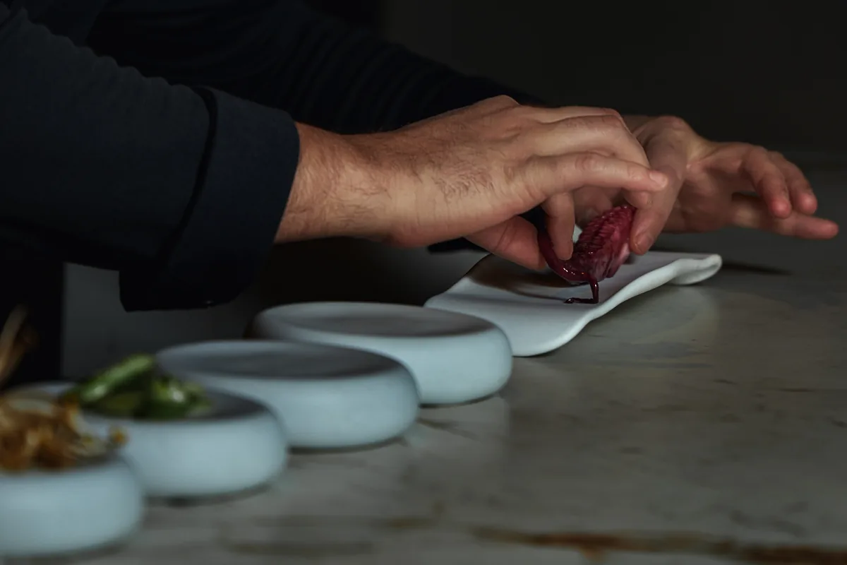 Manos del chef emplatando junto a una fila de cuencos blancos