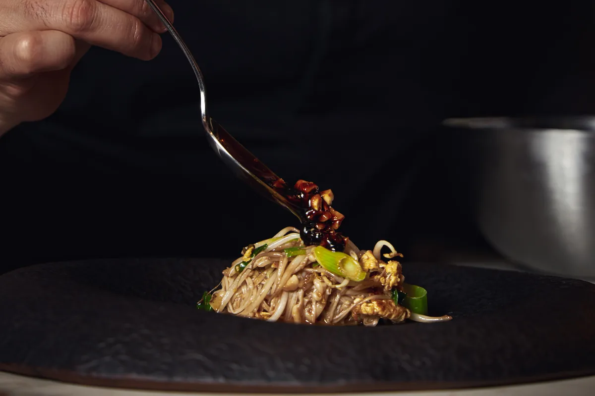 Salsa cayendo desde la cuchara sobre un plato de noodles en plato negro