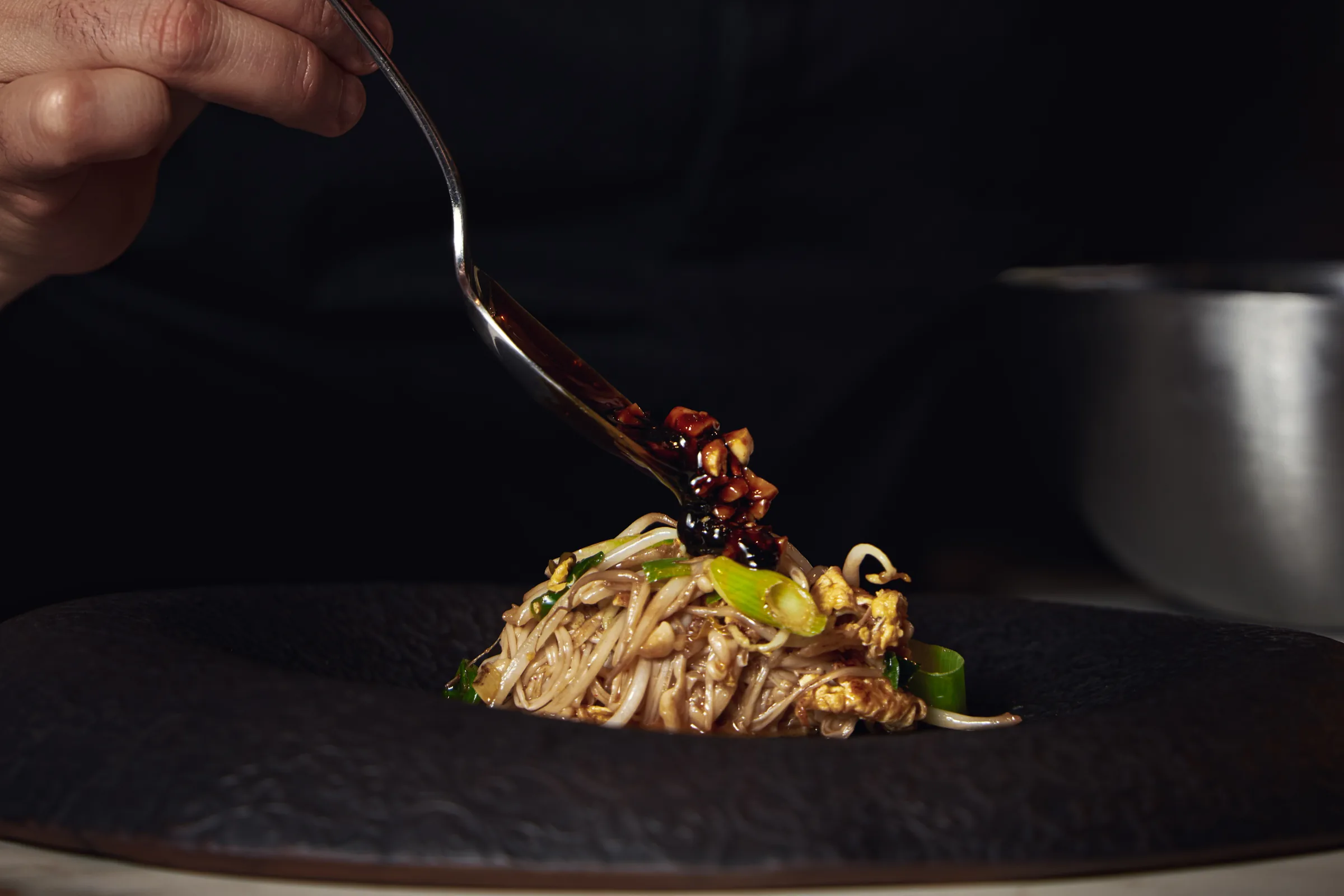 Salsa cayendo desde la cuchara sobre un plato de noodles en plato negro